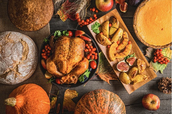 Overhead shot of Thanksgiving table with a turkey, grilled fruit, pumpkin pie, bread and other baked goods, pumpkins and fall decorations
