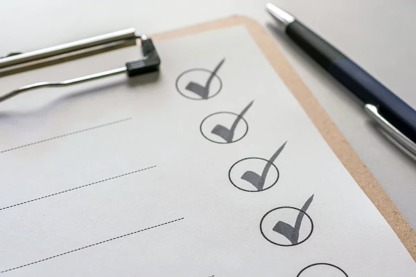 A checklist on a clipboard with several items ticked off and a pen lying beside it.