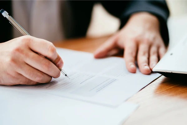 A person is signing a document on a wooden table.
