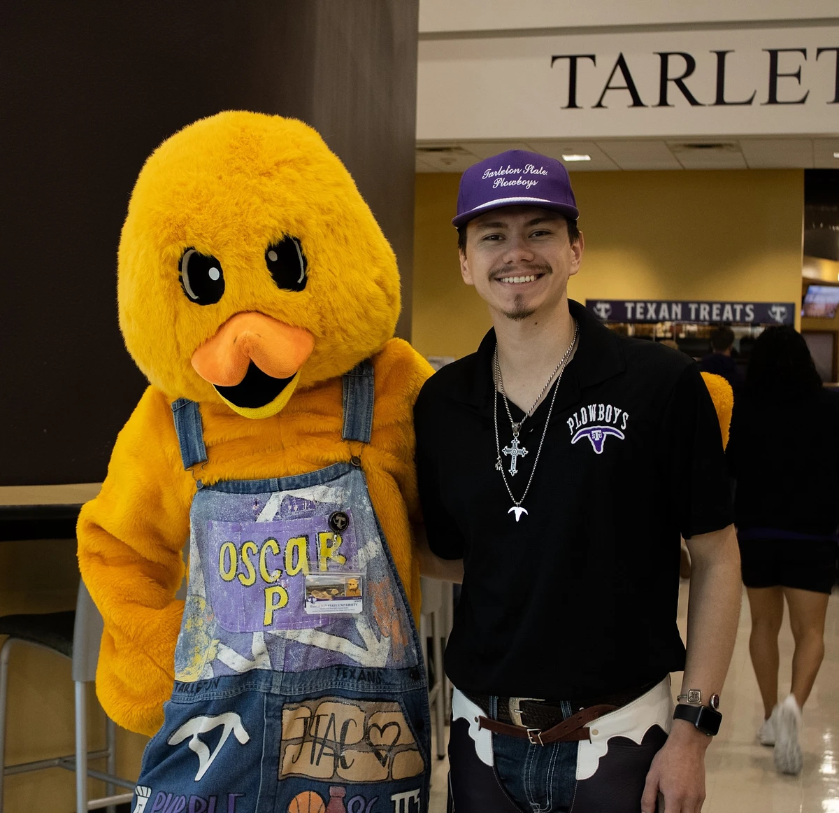 Yellow duck mascot standing next to a student in the dining hall.